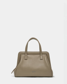 The Rudsak TAULLA - 8325002 Almond is a women’s pebble leather satchel in taupe with two handles, a structured rectangular design, metallic brand lettering on the front, and a spacious interior, shown against a plain white background.