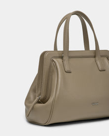 The Rudsak TAULLA - 8325002 Almond is a taupe women’s pebble leather satchel with double handles, a structured rectangular shape, removable shoulder strap, and subtle metallic branding. Stylish and practical, shown on a plain white background.