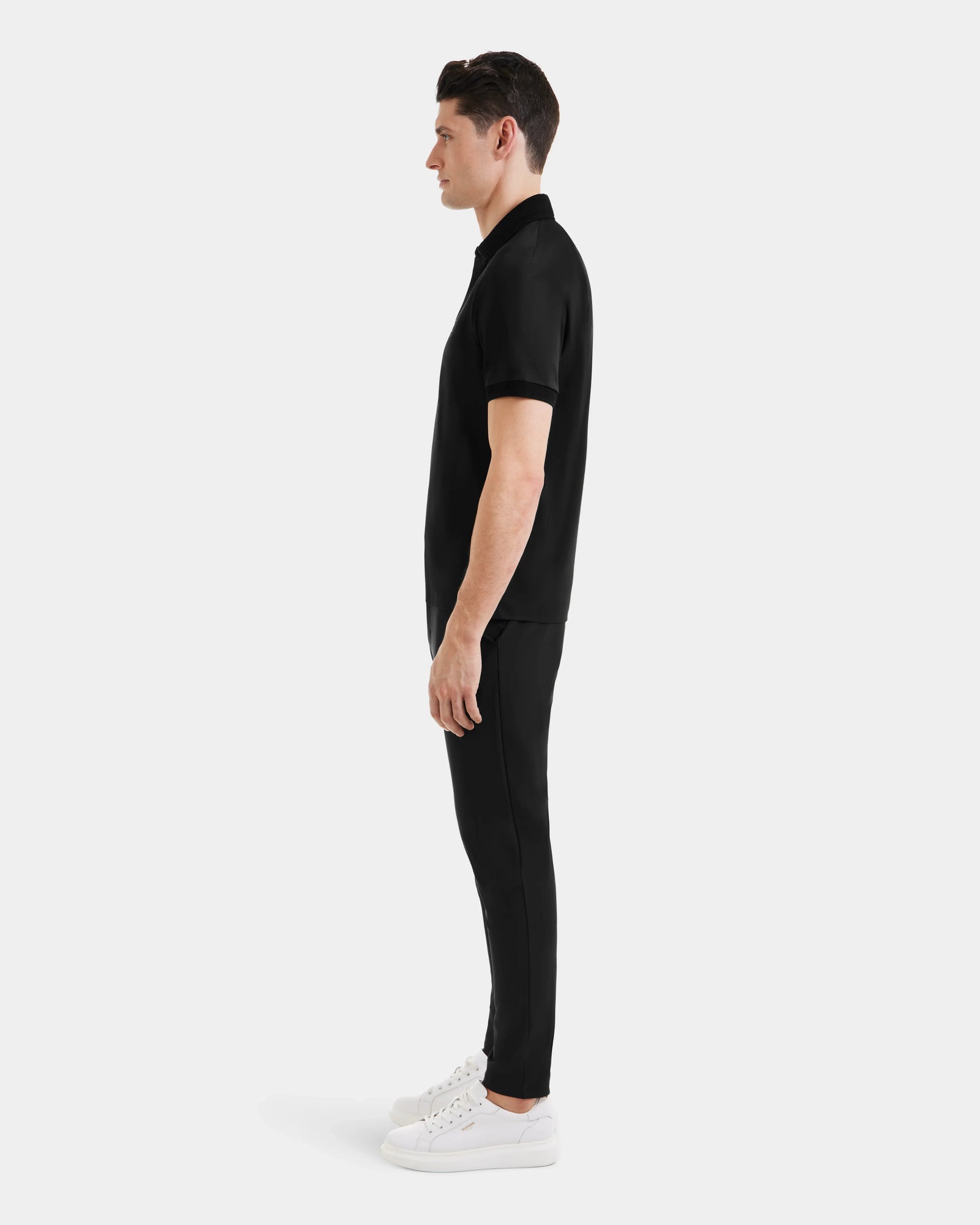 A man wearing the WALTER - 6524531 Black/Black premium cotton polo by Rudsak and black pants.