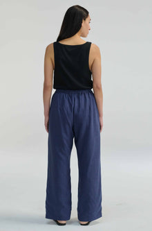Woman wearing a black sleeveless top and blue pants on a light gray background