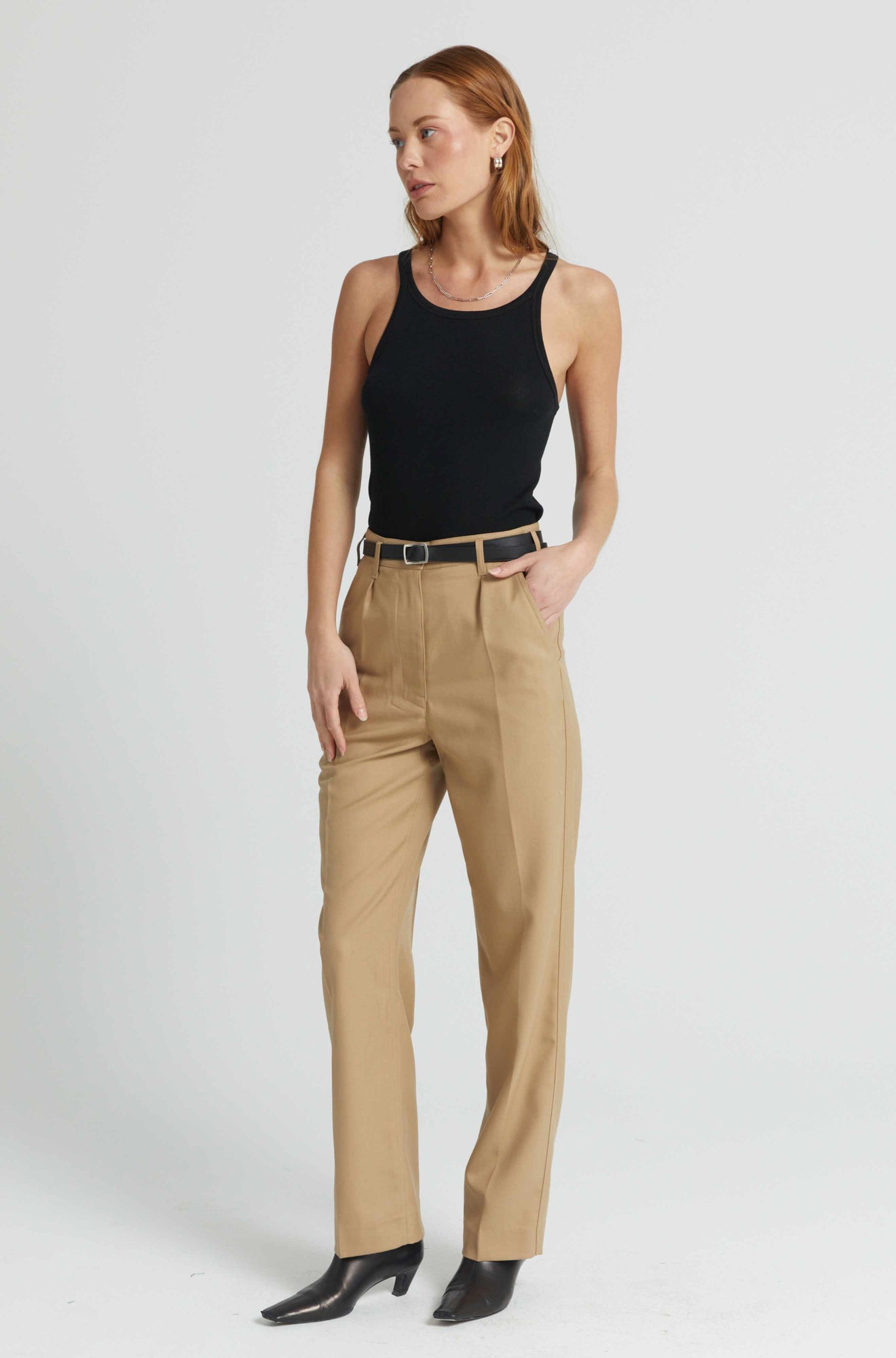 Woman wearing a black tank top and beige pants on a white background