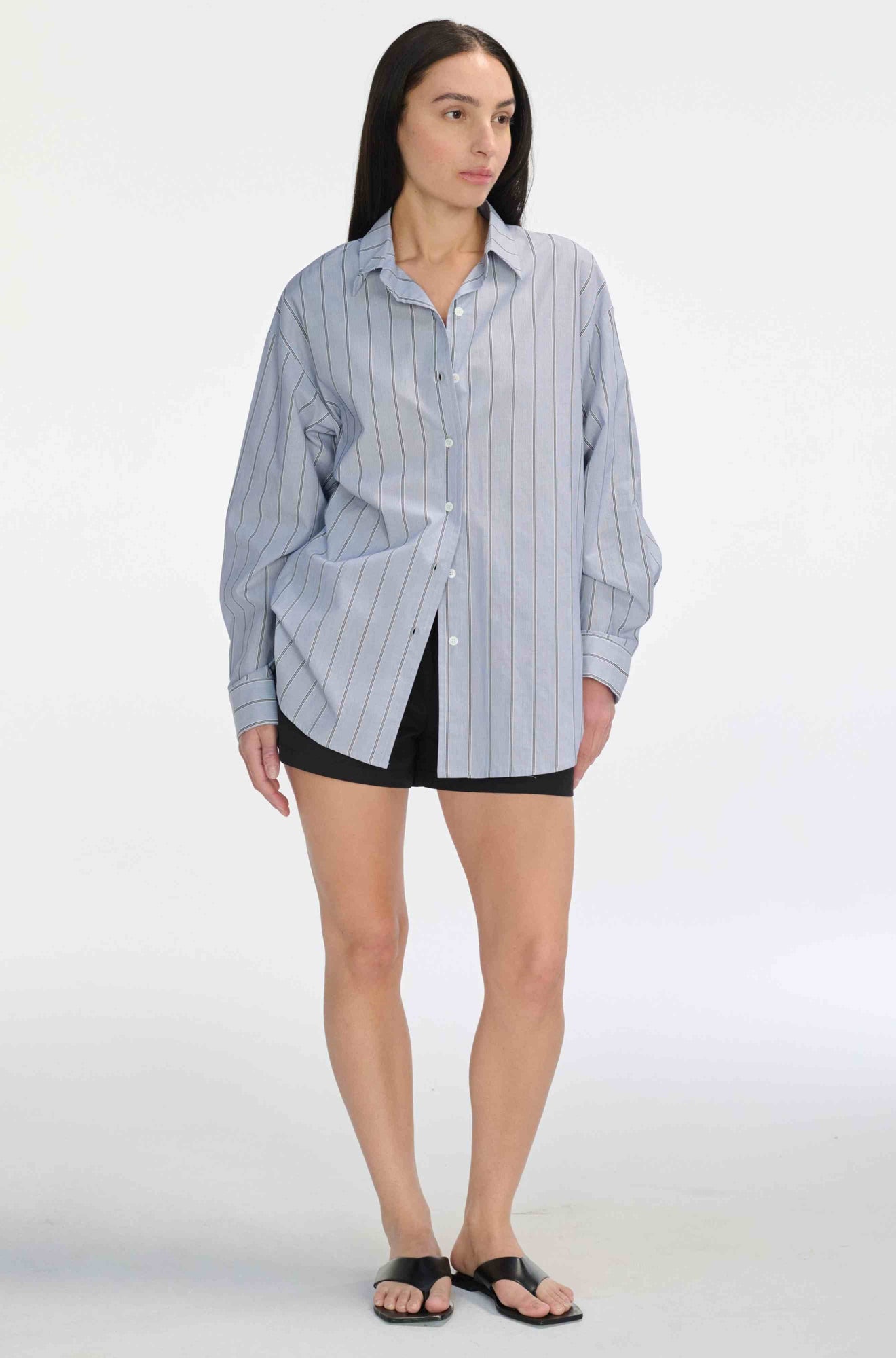 Woman wearing a black and navy striped shirt with black shorts against a light grey background