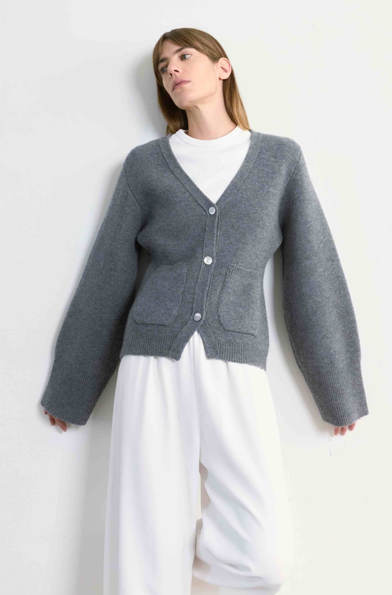 Person wearing a gray cardigan over a white shirt and pants on a light background