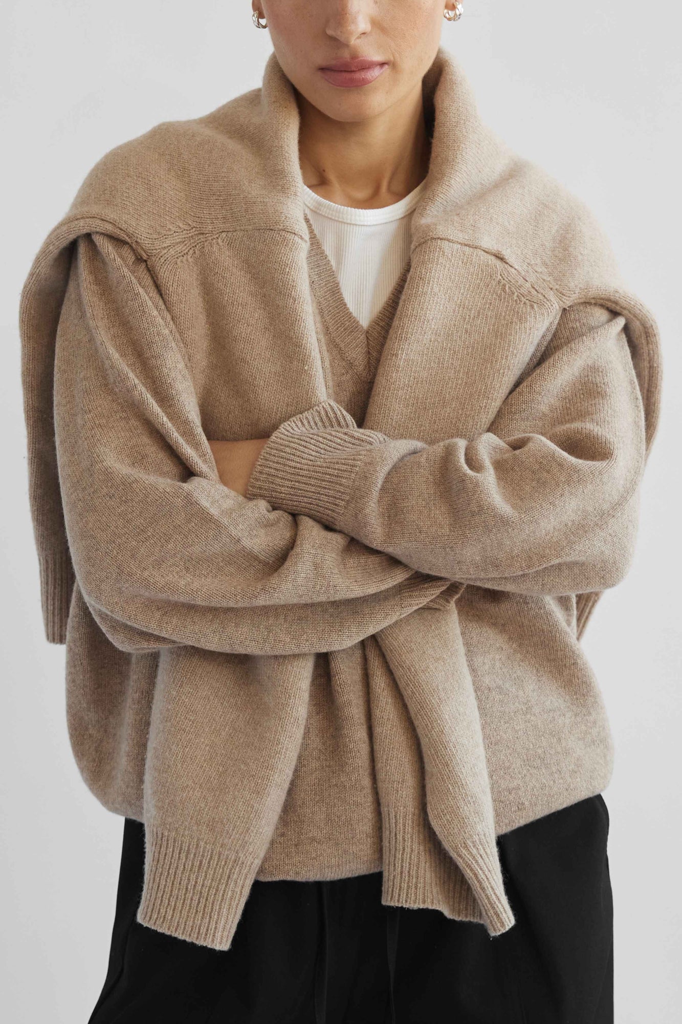 Person wearing a beige cardigan over a white shirt on a light gray background