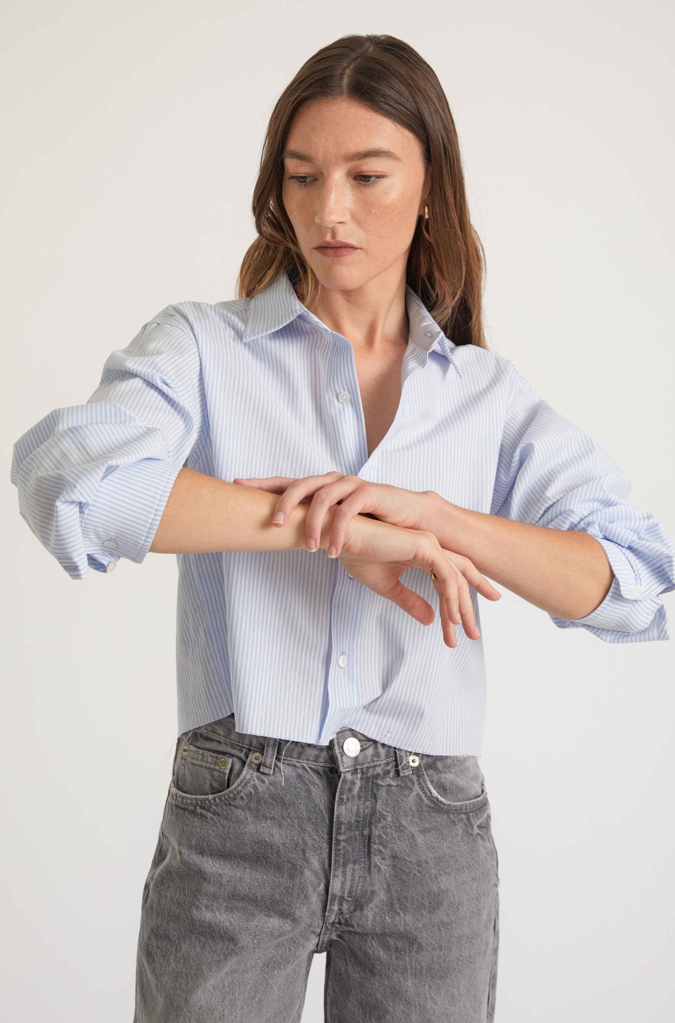 Woman wearing a light blue checkered shirt and gray jeans against a white background