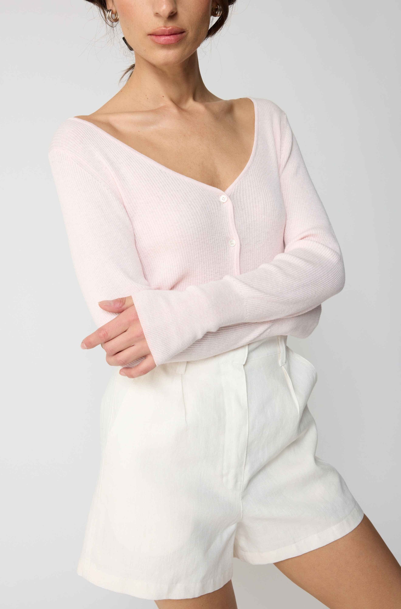 Person wearing a light pink long-sleeve top and white shorts on a plain background