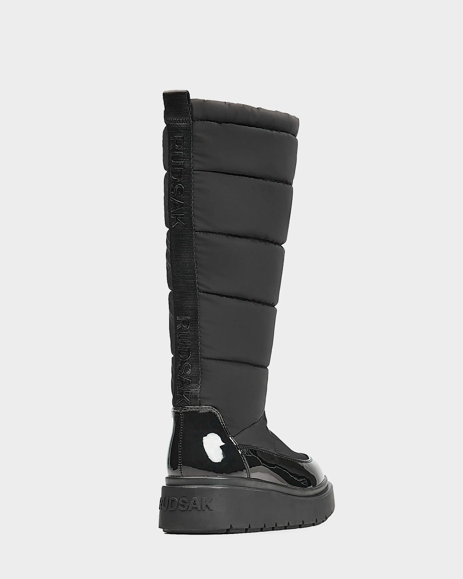 A single black Rudsak CLAUDE - L223506 women's tall quilted winter boot featuring a thick textured sole, glossy toe and heel accents, and a vertical rear pull tab with raised RUDSAK branding.
