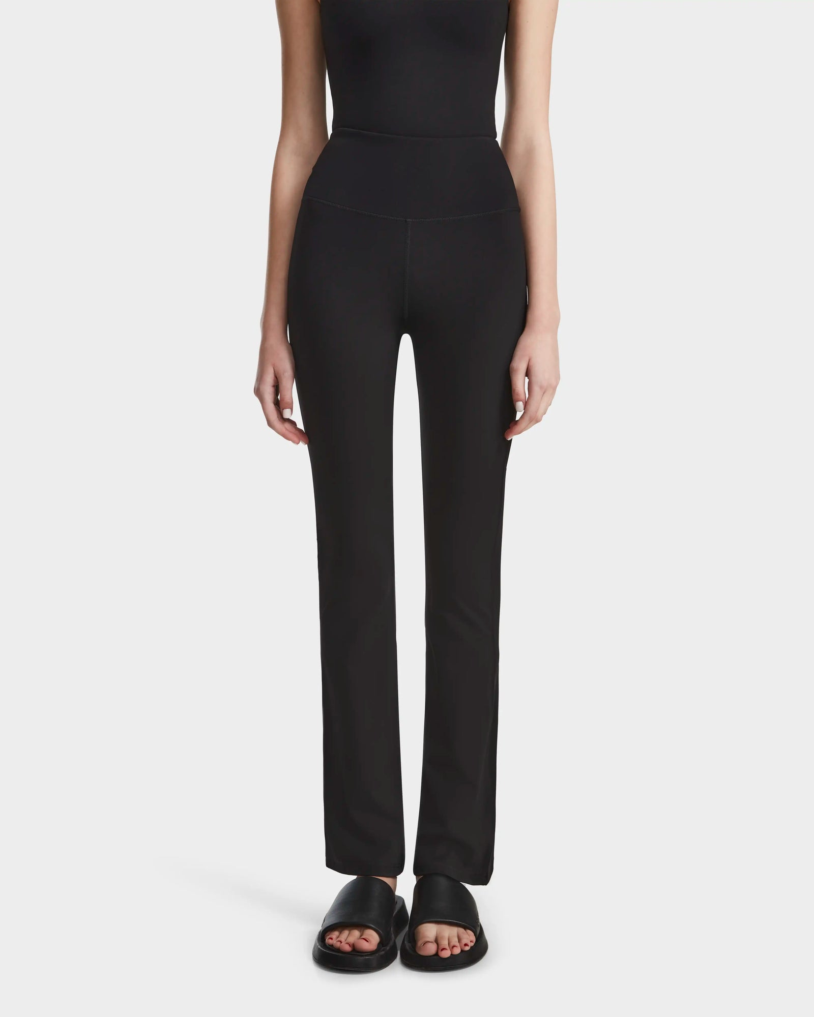 A person wearing the Rudsak ADRIANA - 8524009 Black top and fitted black leggings stands against a plain light background. Only the body from shoulders down is visible; black slide sandals complete the look.