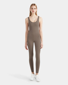A woman faces forward in the Rudsak JEWEL - 8524032 Cement womens sleeveless stretch jumpsuit, fitted and paired with white sneakers, set against a plain white background.