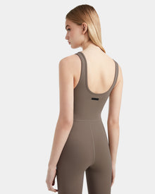 A woman with straight blonde hair models the Rudsak JEWEL - 8524032 Cement, a taupe sleeveless stretch jumpsuit, standing against a plain white background and looking to her right.