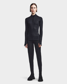 A person with short brown hair faces forward, wearing the Rudsak SIRE - 8523531 Black Pattern ski top, black leggings, and black lace-up boots against a plain light background—ideal for cold weather fashion.