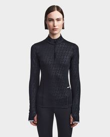 A woman with straight brown hair models the Rudsak SIRE - 8523531 Black Pattern fitted, fleece-lined jersey ski top with a subtle geometric print and short front zipper against a plain light gray background—ideal for cold weather.