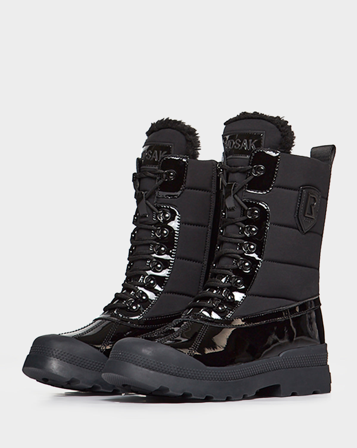 The Rudsak LEX - 8222501 BLACK women’s winter boots feature black patent panels, thick rubber soles, insulated padded uppers, metal eyelets, faux fur trim, and a side emblem—perfect for staying warm and stylish.