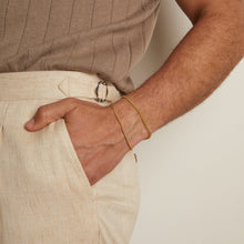 Model. Person wearing a brown ribbed top and beige pants with a gold bracelet on a neutral background