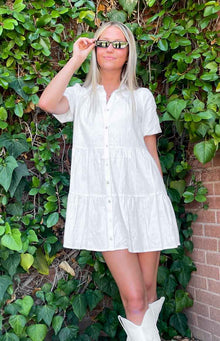 Front view of a white linen tiered mini dress with a collared V-neck and full button-front