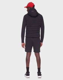 A person facing away wears the RUDSAK JAS - 6122006 BLACK men’s windbreaker, paired with black shorts, black socks, black and white sneakers, and a red cap against a plain white background.