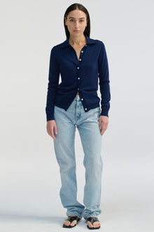 Woman wearing a navy blue button-up shirt and light blue jeans on a white background