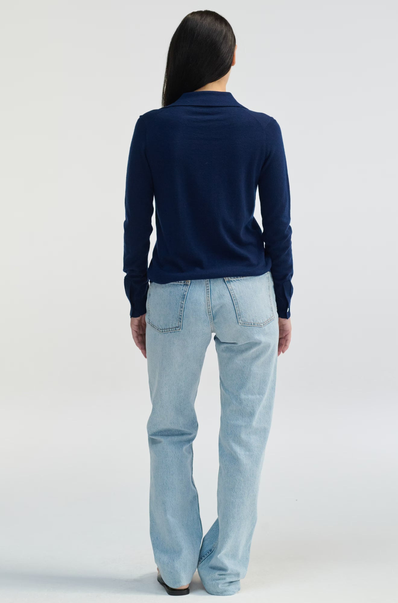 Person wearing a navy sweater and light blue jeans on a white background